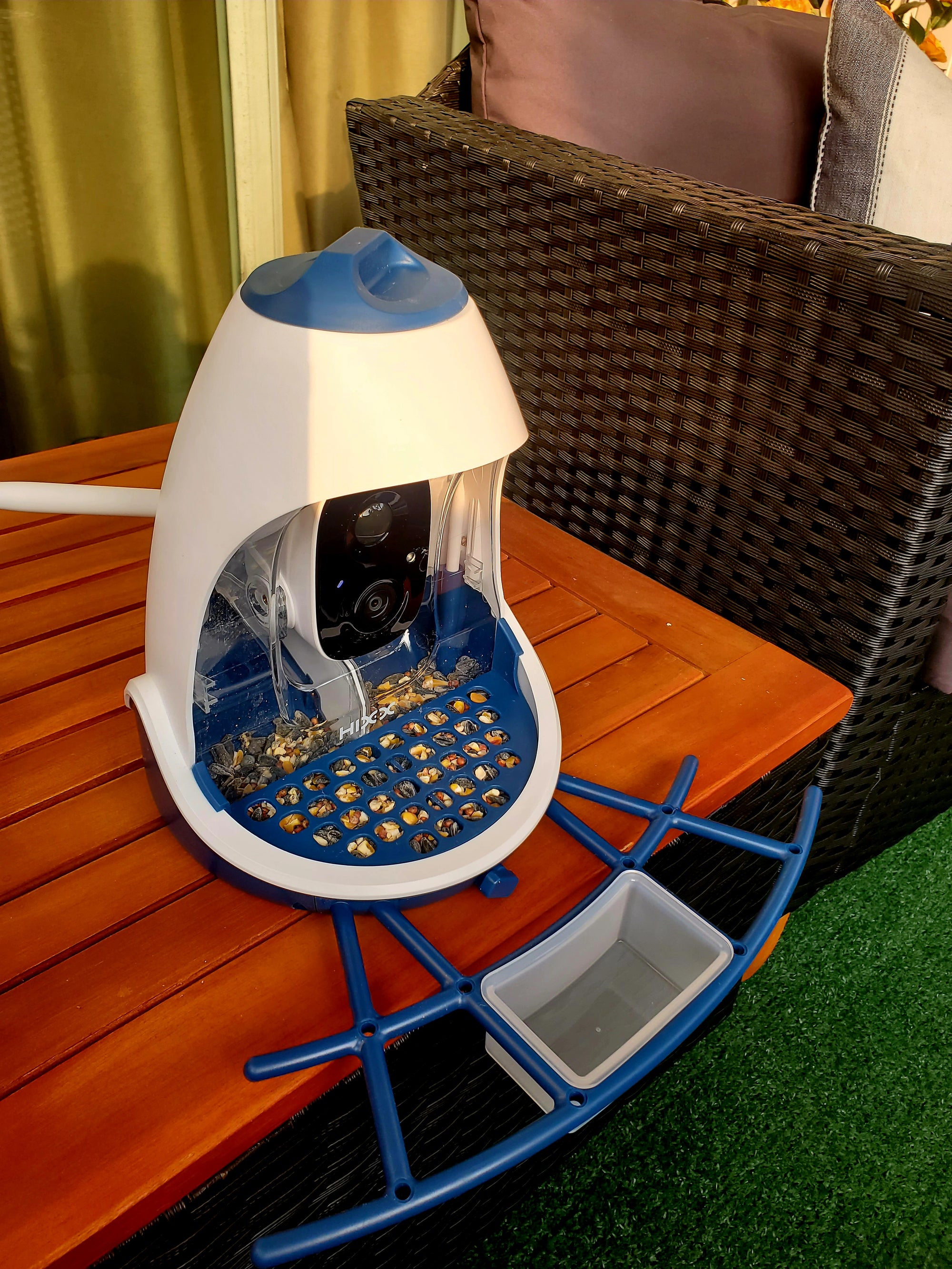 Hixx Smart Bird Feeder Camera & Seed Guard in white and blue on patio table, featuring 2.5K HD camera, AI bird ID, and squirrel-proof design.