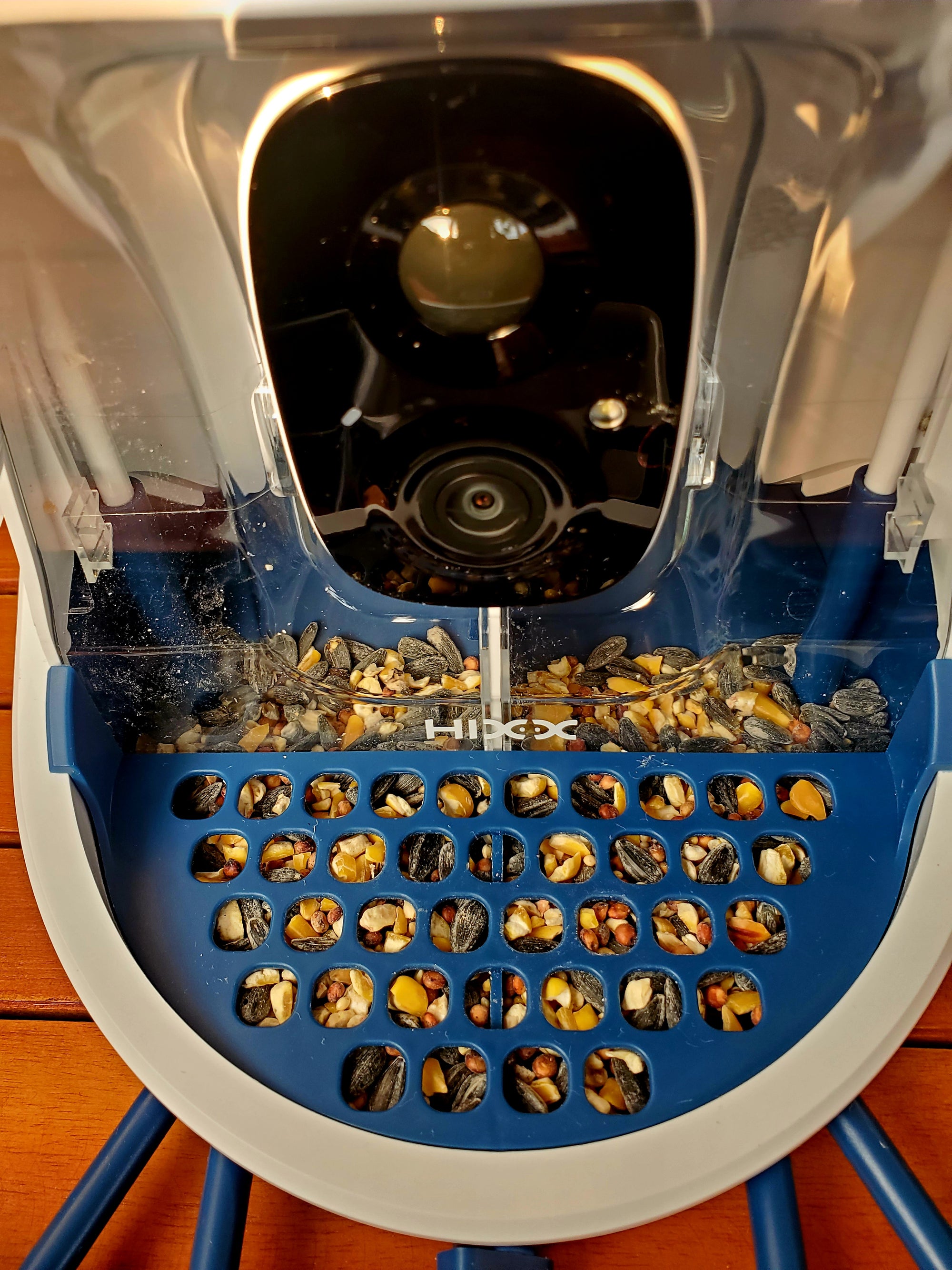 Hixx Smart Bird Feeder Camera & Seed Guard in blue with 2.5K HD camera and seed tray filled with mixed birdseed. Ideal for wild bird watching.